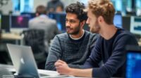 Zwei IT-Mitarbeiter besprechen an einem Computerarbeitsplatz mögliche Maßnahmen bei einer kritischen PHP-Sicherheitslücke.
